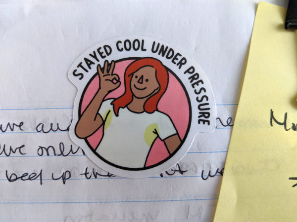 Round sticker that says "stayed cool under pressure" with a woman in a pit-stained t-shirt giving the okay finger sign